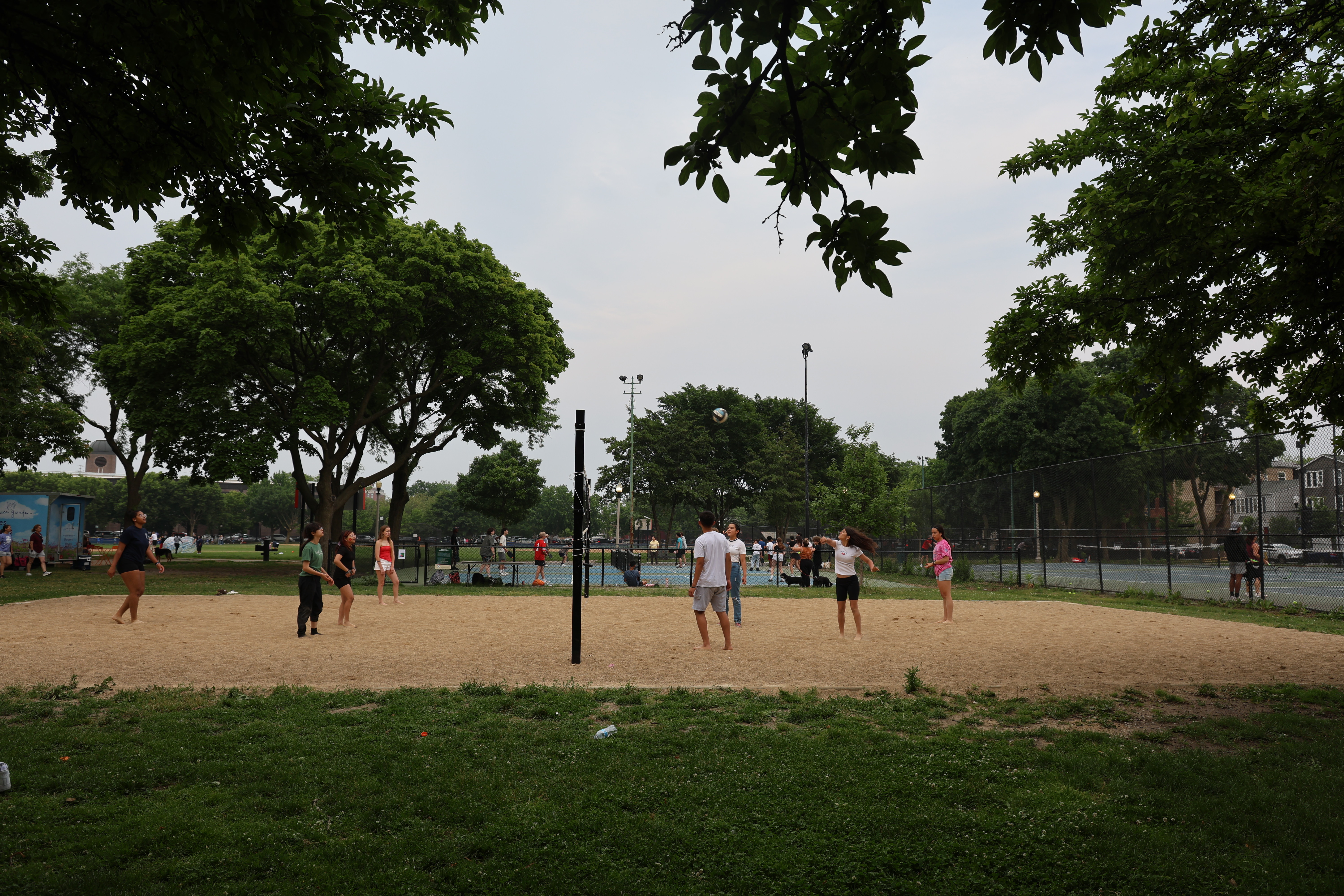 People play volleyball on a sand court in a park.